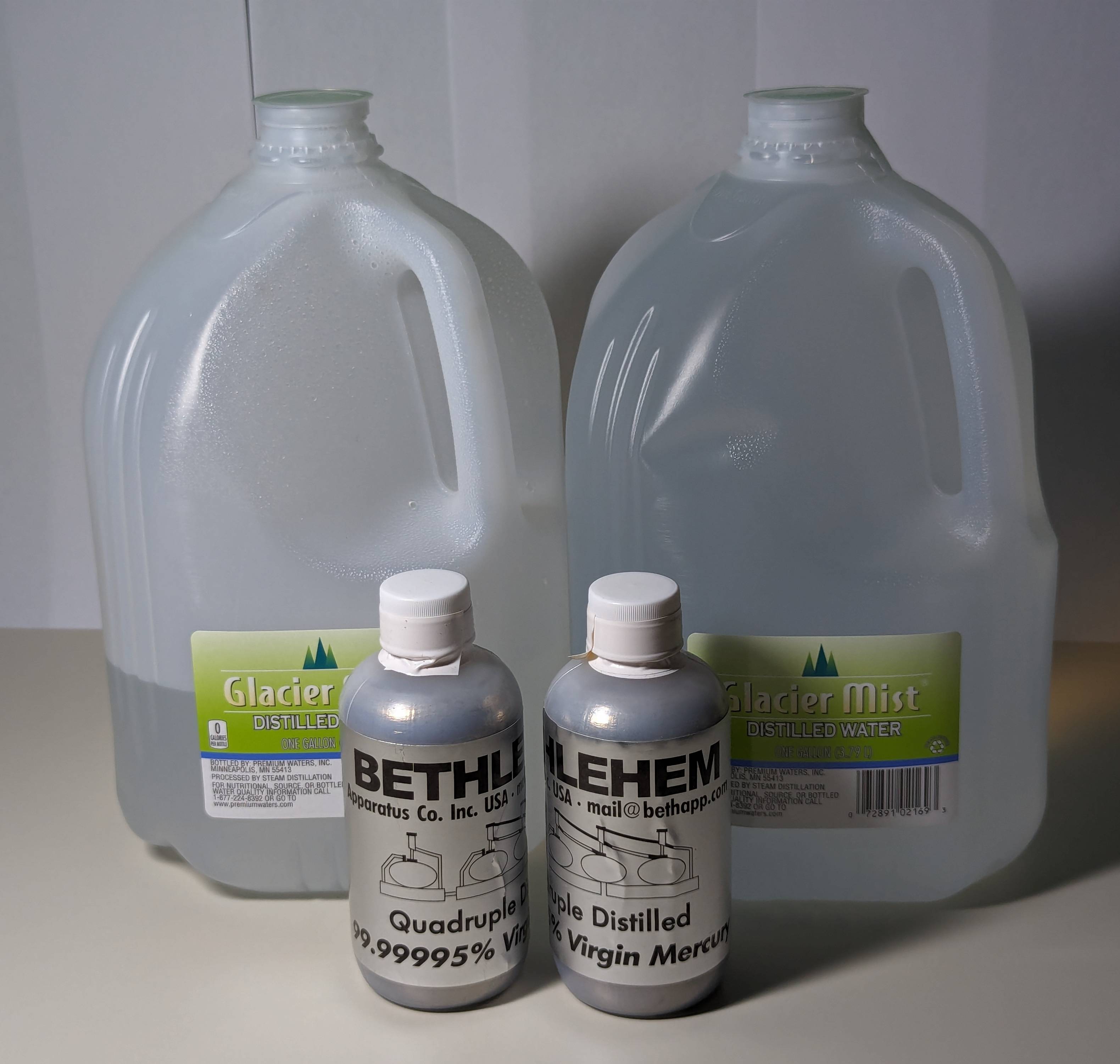 Two 200 mL bottles of mercury sit in front of two gallon jugs of water, one jug full and the other about a third full.